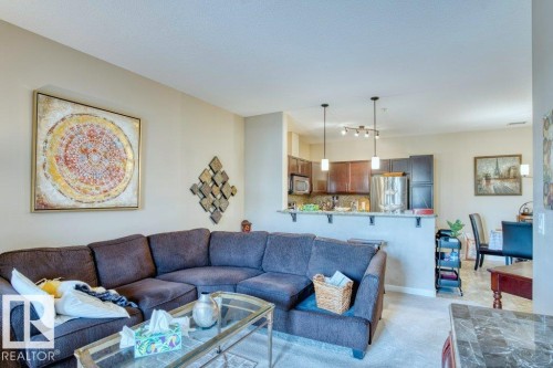 Open-concept living space featuring a kitchen with dark wood-finish cabinetry, a built-in microwave, and a breakfast bar with pendant lighting - 319 6083 Maynard Way, Edmonton, AB 