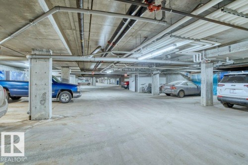 Underground parking facility featuring concrete construction, exposed utility piping, and fluorescent lighting - 319 6083 Maynard Way, Edmonton, AB 