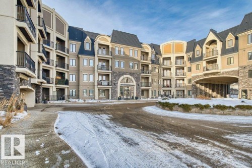 Multi-story building featuring stone veneer accents, stucco siding, a gabled roofline, and individual balconies with black railings - 319 6083 Maynard Way, Edmonton, AB 