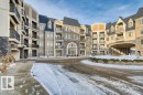 Multi-story building featuring stone veneer accents, stucco siding, a gabled roofline, and individual balconies with black railings - 319 6083 Maynard Way, Edmonton, AB 