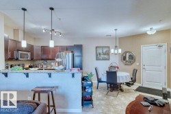 Kitchen and dining area featuring dark wood-finish cabinetry, stainless steel appliances, a stone-finish countertop with a breakfast bar, and a pendant light fixture - 