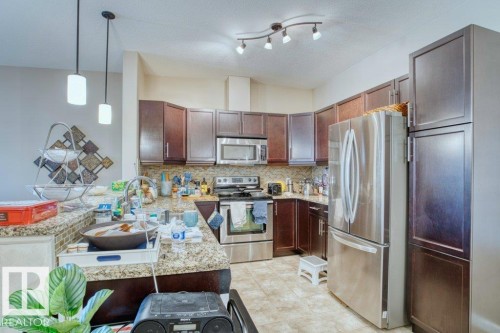 Kitchen featuring dark wood-finish cabinetry, stainless steel appliances, granite countertops, and a tile backsplash - 319 6083 Maynard Way, Edmonton, AB 