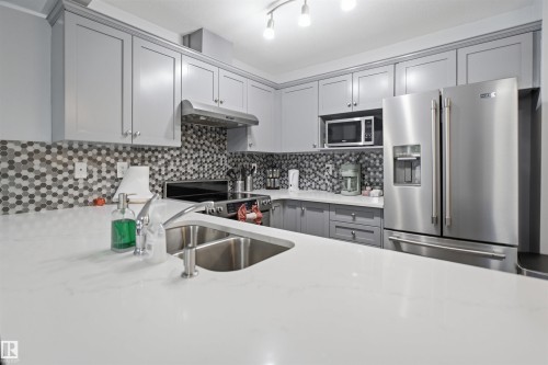 Kitchen featuring white countertops, grey shaker-style cabinetry, and a mosaic tile backsplash - 92 230 Edwards Drive, Edmonton, AB 