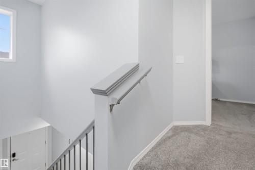 Staircase featuring painted wooden newel post, metal balusters, and a light gray handrail - 92 230 Edwards Drive, Edmonton, AB 