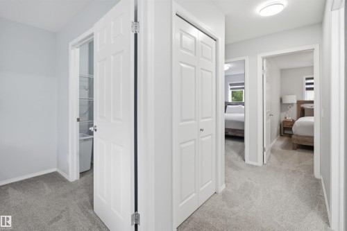 Carpeted hallway featuring white paneled doors, a flush-mount ceiling light, and built-in closet storage - 92 230 Edwards Drive, Edmonton, AB 