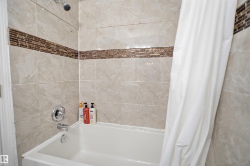 Bathtub with light-toned tiled surround and decorative mosaic accent band - 92 230 Edwards Drive, Edmonton, AB 