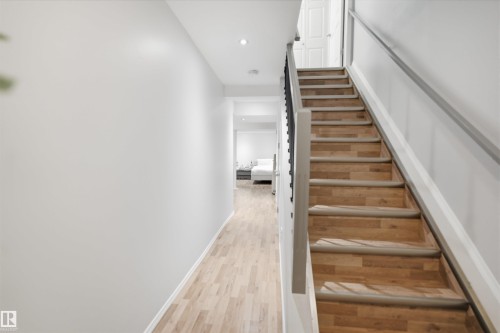 Staircase featuring wood-finish treads and risers, light gray handrails, and white walls - 92 230 Edwards Drive, Edmonton, AB 