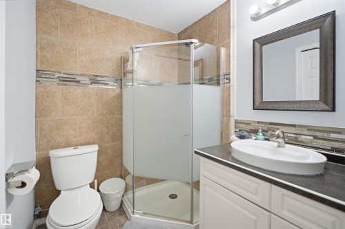 Bathroom featuring a corner shower with glass enclosure, a white vanity with an oval vessel sink, and a framed mirror - 92 230 Edwards Drive, Edmonton, AB 
