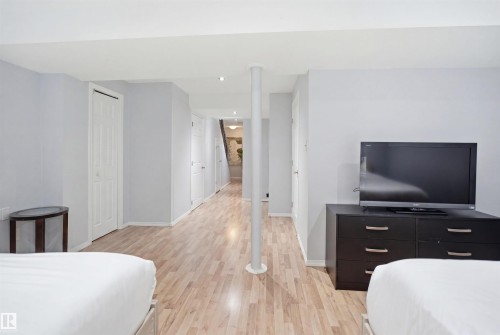 Spacious lower-level room featuring wood-finish flooring, light gray walls, and white trim - 92 230 Edwards Drive, Edmonton, AB 