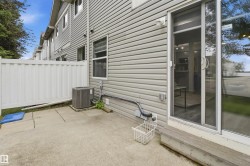 Rear exterior featuring light grey siding, a concrete patio, a white privacy fence, a visible HVAC unit, and a glass sliding door - 