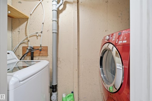 Laundry area with exposed concrete walls, visible plumbing, and wood shelving - 92 230 Edwards Drive, Edmonton, AB 