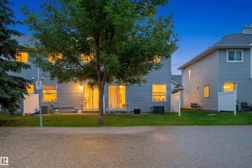 Rear exterior featuring light grey siding, multiple windows, a sliding glass door, and white privacy fencing - 92 230 Edwards Drive, Edmonton, AB 