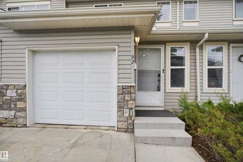 Exterior facade featuring horizontal siding, a white panel garage door, and a stone veneer foundation accent - 92 230 Edwards Drive, Edmonton, AB 