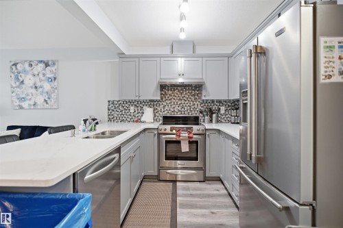 Modern kitchen featuring light gray cabinetry, stainless steel appliances, a mosaic tile backsplash, and light-tone countertops - 92 230 Edwards Drive, Edmonton, AB 