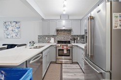 Modern kitchen featuring light gray cabinetry, stainless steel appliances, a mosaic tile backsplash, and light-tone countertops - 