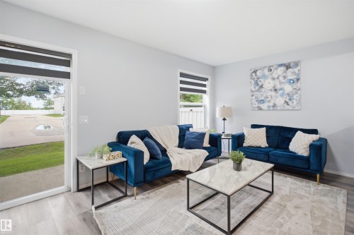 Living area featuring light gray walls, wood-finish flooring, a sliding glass door, and a window with horizontal blinds - 92 230 Edwards Drive, Edmonton, AB 