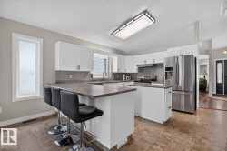 Spacious kitchen featuring white cabinetry, stainless steel appliances, a tiled backsplash, and a multi-purpose island with counter seating - 