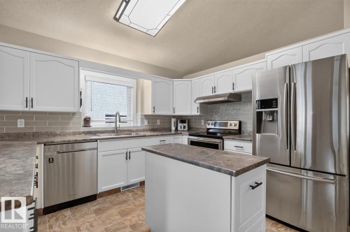 Contemporary kitchen featuring white cabinetry, stainless steel appliances, a center island with a dark countertop, and a tiled backsplash - 448 Ormsby Road W, Edmonton, AB 