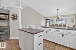 Kitchen featuring a central island, white shaker-style cabinetry with black hardware, and brown-toned tile flooring - 