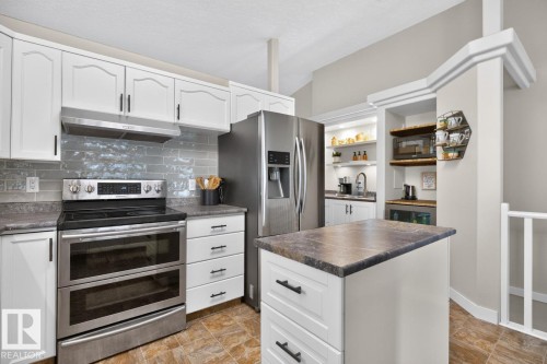 Kitchen featuring white cabinetry, gray subway tile backsplash, stainless steel appliances, and an eat-at island with a dark countertop - 448 Ormsby Road W, Edmonton, AB 