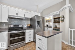 Kitchen featuring white cabinetry, gray subway tile backsplash, stainless steel appliances, and an eat-at island with a dark countertop - 