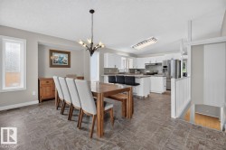 Open-concept dining and kitchen area featuring tile flooring, white cabinetry, stainless steel appliances, a kitchen island with seating, and a decorative chandelier - 