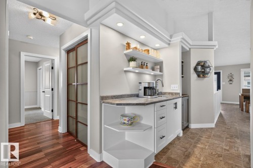 Integrated wet bar featuring a single-basin sink, stone-finish countertop, white cabinetry with dark hardware, and recessed lighting - 448 Ormsby Road W, Edmonton, AB 