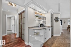 Integrated wet bar featuring a single-basin sink, stone-finish countertop, white cabinetry with dark hardware, and recessed lighting - 