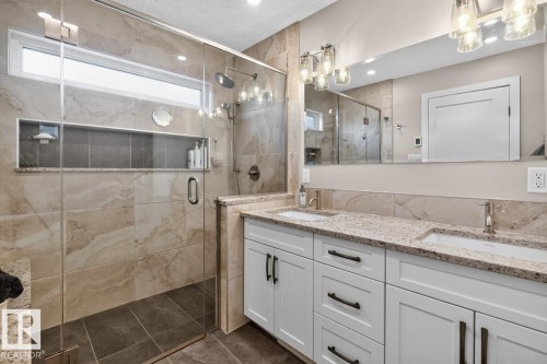 Bathroom featuring a glass-enclosed shower with stone-look tile, a recessed niche, and a horizontal window - 448 Ormsby Road W, Edmonton, AB 
