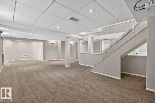Finished lower level featuring neutral carpeting, recessed lighting, drop ceiling, and a painted staircase with metal handrail - 448 Ormsby Road W, Edmonton, AB 
