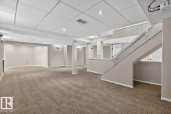 Finished lower level featuring neutral carpeting, recessed lighting, drop ceiling, and a painted staircase with metal handrail - 