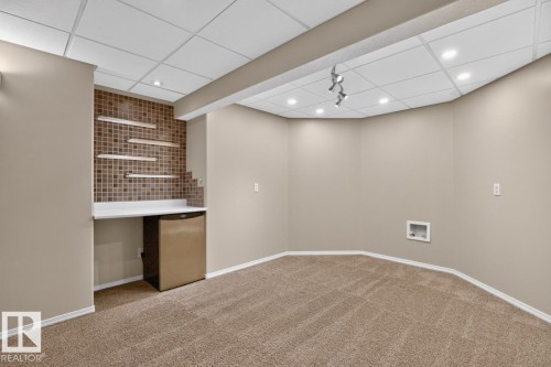 Finished basement featuring a built-in wet bar with a tiled backsplash, floating shelves, and a solid surface countertop - 448 Ormsby Road W, Edmonton, AB 