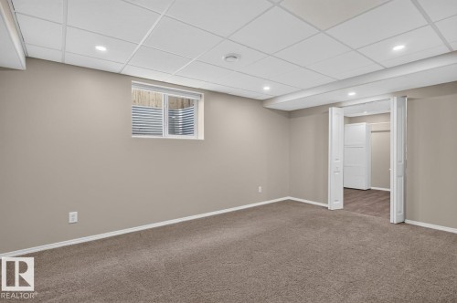 Spacious room featuring neutral carpeting, light-toned walls, and a drop ceiling with recessed lighting - 448 Ormsby Road W, Edmonton, AB 