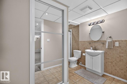 Bathroom featuring a contemporary vanity with an integrated sink, ceramic tile flooring, and wainscoting - 448 Ormsby Road W, Edmonton, AB 