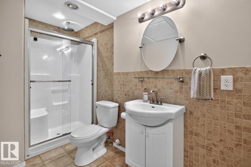 Bathroom featuring a stand-up shower with sliding glass doors, a white toilet, and a vanity with a white basin sink - 448 Ormsby Road W, Edmonton, AB 