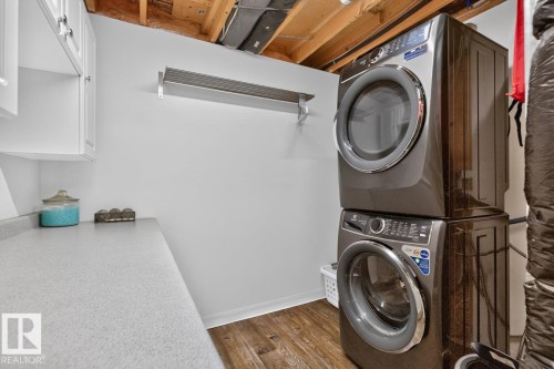 Laundry area featuring wood-finish flooring, white cabinetry, and a stacked washer and dryer unit - 448 Ormsby Road W, Edmonton, AB 