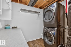 Laundry area featuring wood-finish flooring, white cabinetry, and a stacked washer and dryer unit - 