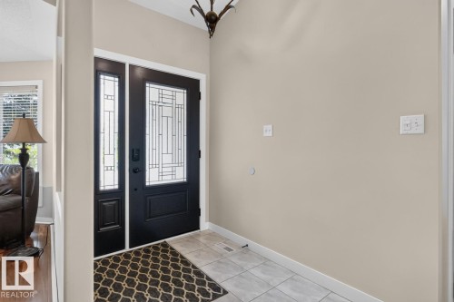 Entryway featuring a black paneled door with decorative glass, a coordinating sidelight, light neutral wall paint, and ceramic tile flooring - 448 Ormsby Road W, Edmonton, AB 