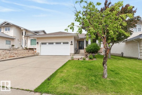 Front exterior featuring a two-car garage with paneling, concrete driveway, and a manicured lawn - 448 Ormsby Road W, Edmonton, AB 
