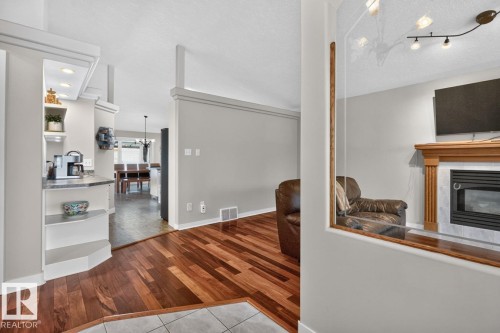 Open concept living area featuring wood-finish flooring, a built-in fireplace with a light wood mantel, and a tiled hearth - 448 Ormsby Road W, Edmonton, AB 