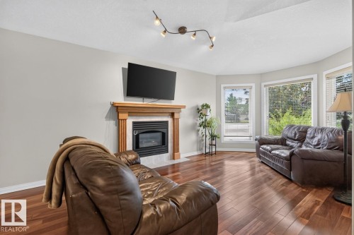 Living area featuring wood-finish flooring, a fireplace with a light-toned wood mantel and tiled surround, and multiple bay windows - 448 Ormsby Road W, Edmonton, AB 