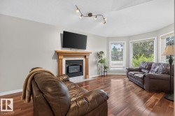 Living area featuring wood-finish flooring, a fireplace with a light-toned wood mantel and tiled surround, and multiple bay windows - 