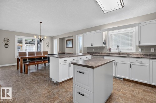Open-concept kitchen and dining area featuring white cabinetry, dual islands with stone-finish countertops, subway tile backsplash, and tile flooring - 448 Ormsby Road W, Edmonton, AB 