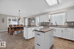 Open-concept kitchen and dining area featuring white cabinetry, dual islands with stone-finish countertops, subway tile backsplash, and tile flooring - 