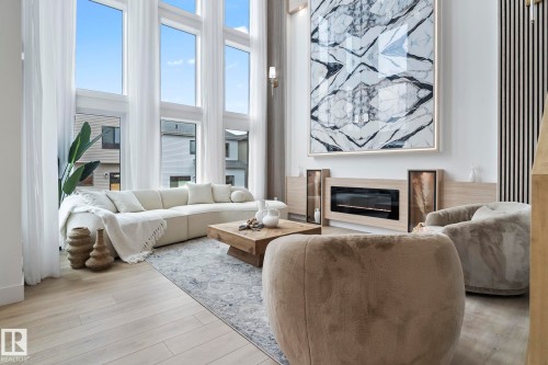 Living area featuring expansive floor-to-ceiling windows, a built-in electric fireplace with a light wood-finish surround, wood-finish flooring, and a panel accent wall - 13152 187 Avenue, Edmonton, AB 