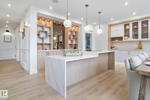 Open-concept kitchen featuring a waterfall island with a fluted wood base, light wood-finish flooring, recessed lighting, and stylish pendant light fixtures - 13152 187 Avenue, Edmonton, AB 