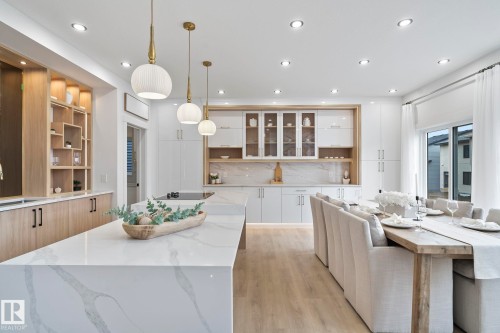 Open-concept kitchen and dining area featuring a waterfall-edge island with an integrated cooktop, pendant lighting, built-in shelving with accent lighting, and wood-finish flooring - 13152 187 Avenue, Edmonton, AB 