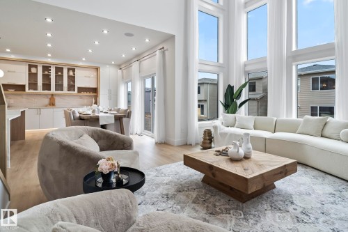 Two-story living area with expansive windows, light wood-finish flooring, recessed lighting, and a modern kitchen with light cabinetry and a stone backsplash - 13152 187 Avenue, Edmonton, AB 