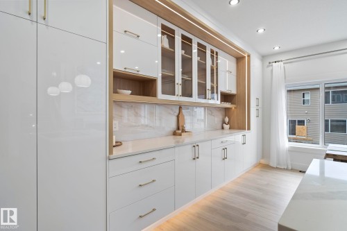 Integrated white cabinetry with gold-tone hardware, wood-finish shelving, glass-front upper cabinets, and a white countertop with a complementing backsplash - 13152 187 Avenue, Edmonton, AB 