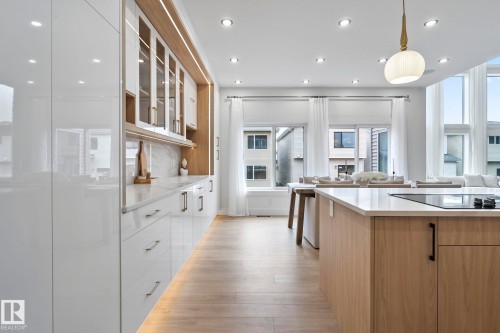 Modern kitchen featuring a large island with an integrated cooktop, wood-finish flooring, recessed lighting, and expansive windows - 13152 187 Avenue, Edmonton, AB 